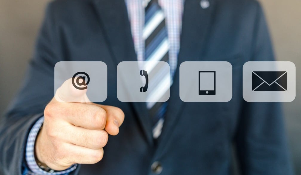 Man in suit and tie pointing at email, phone and tablet icons