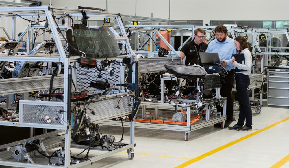 Two men and one woman looking at a laptop inside a manufacturing building