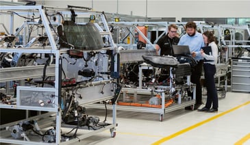 Two men and one woman looking at a laptop inside a manufacturing building